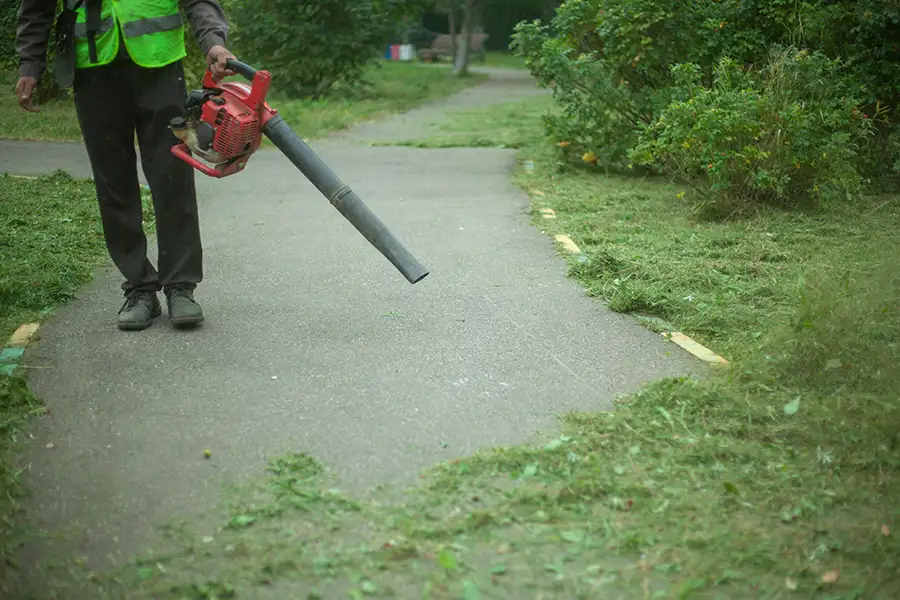 professional using leaf blower to clear concrete path of mulched grass from lawncare maintenance - Springfield, IL
